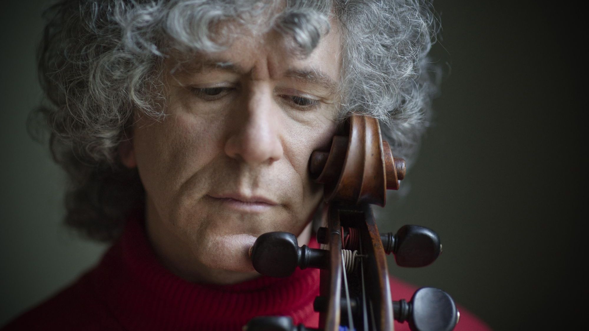 Foto von Steven Isserlis – Nahaufnahme vom Gesicht des Cellisten, der seine Wange gegen die Schnecke seines Cellos hält und nach unten blickt
