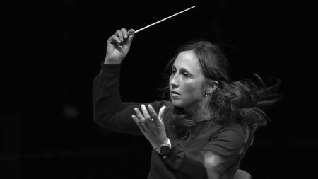 Foto von Joana Carneiro – Halbtotale der Dirigentin, die gerade im schwarzen Hemd mitten in einem Konzert mit Taktstock in der Hand dirigiert