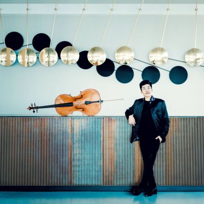 Foto von Bryan Cheng – Totale des Cellisten, angelehnt an einer langen Kommode, dort liegt sein Cello drauf