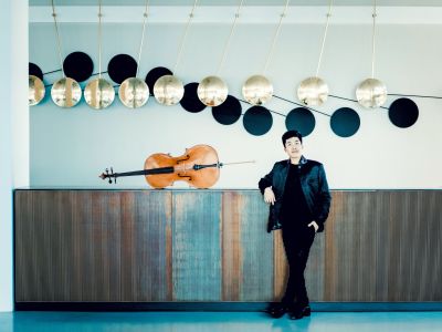 Foto von Bryan Cheng – Totale des Cellisten, angelehnt an einer langen Kommode, dort liegt sein Cello drauf
