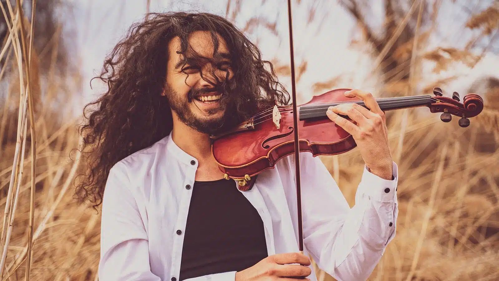 Foto von Nemanja Radulović – der Geiger steht draussen und spielt lachend und mit wehendem, dunklem und lockigem Haar auf seiner Geige