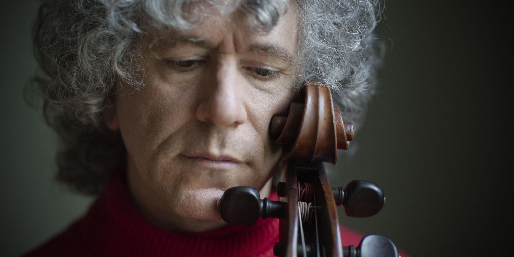 Foto von Steven Isserlis – Nahaufnahme vom Gesicht des Cellisten, der seine Wange gegen die Schnecke seines Cellos hält und nach unten blickt