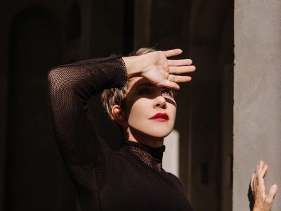 Foto von Joyce DiDonato – Die Mezzosopranistin in dramatischer Pose, mit der Hand vor der Sonne, in einem schwarzen Outfit.