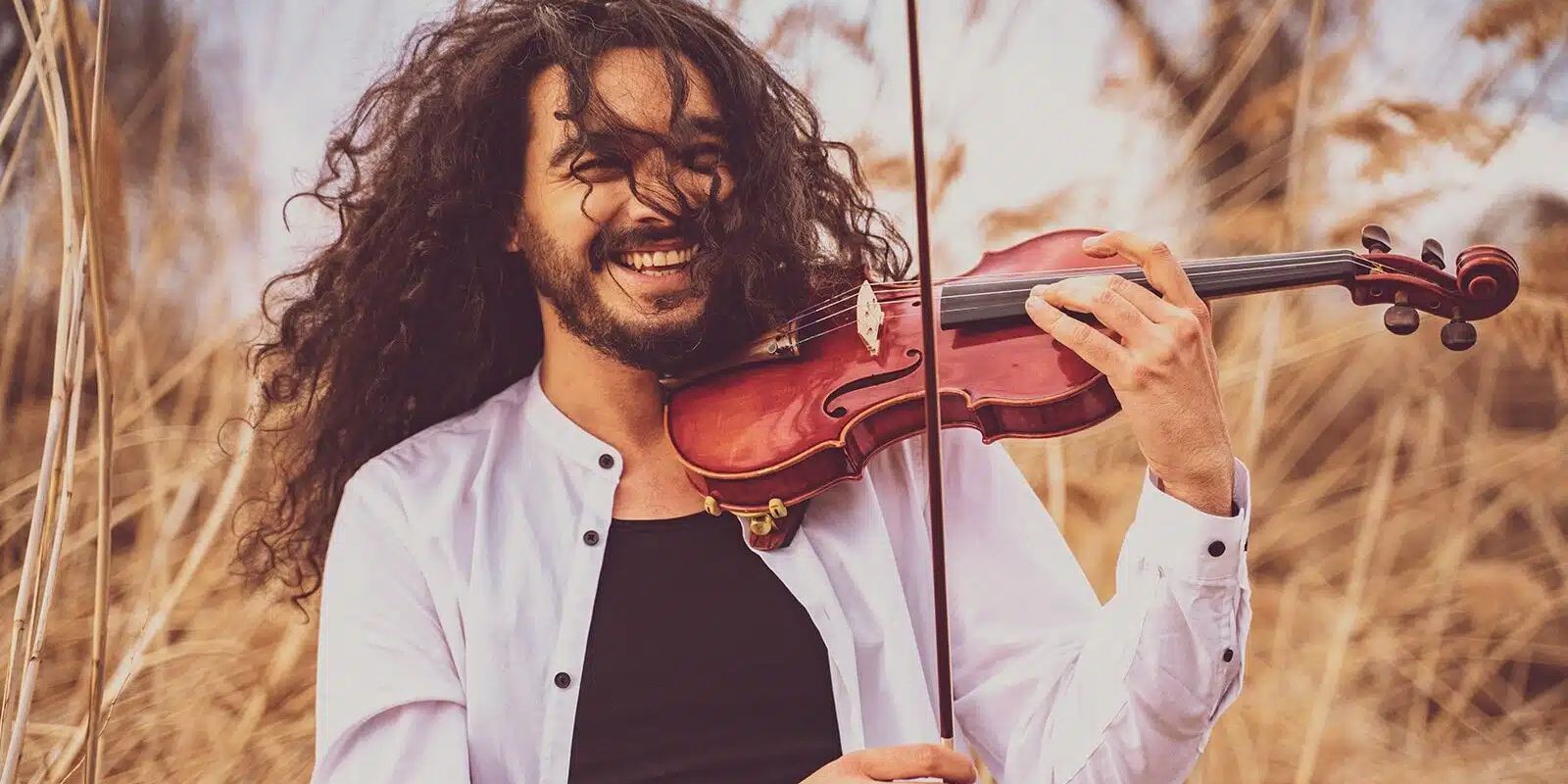 Foto von Nemanja Radulović – der Geiger steht draussen und spielt lachend und mit wehendem, dunklem und lockigem Haar auf seiner Geige